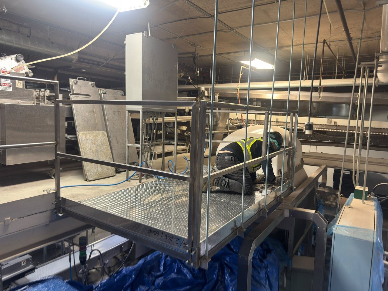Elevated walkway platform with diamond plate decking and guardrails above conveyor machinery, GTA industrial facility